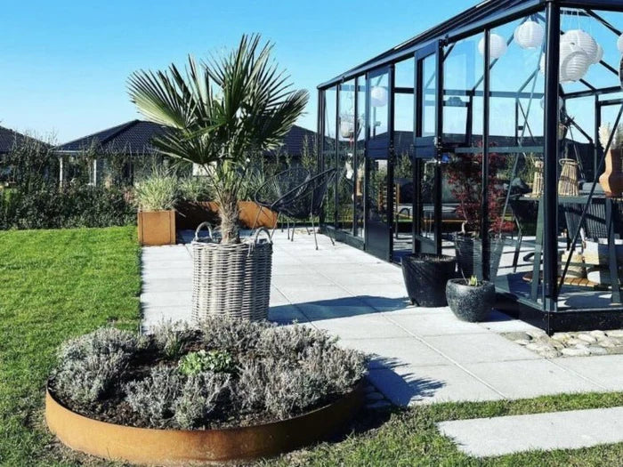 Bedkant i cortenstål med planter foran drivhus