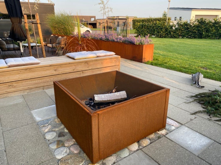 Firkantet bålplass i cortenstål plassert i hage, omgitt av terrasse og beplantning