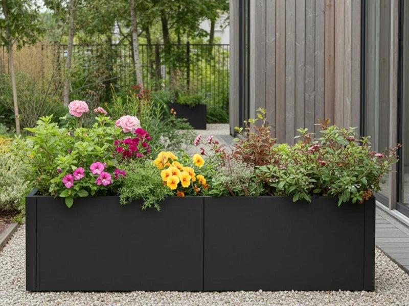 Lang plantekasse i svart stål med blomstrende planter i hage