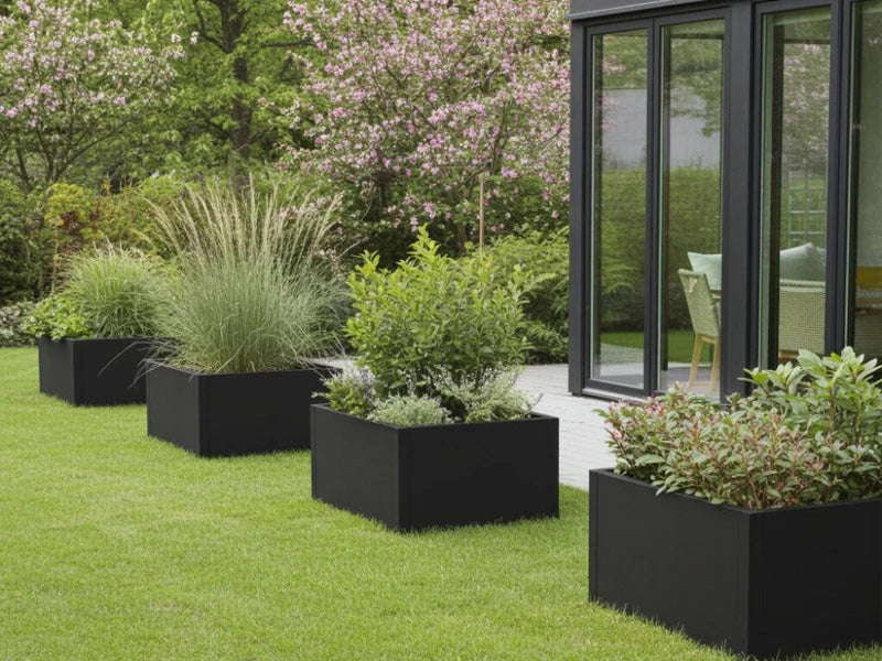 Plantekasser i svart stål med prydgress og busker plassert på plen