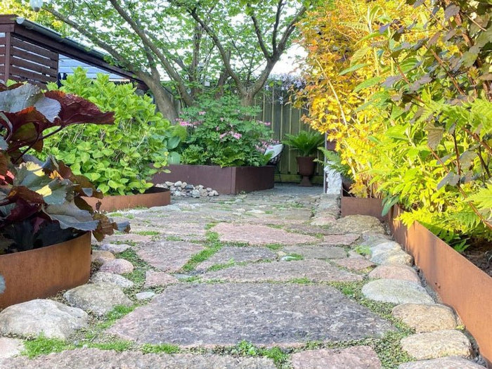 Bedringer i cortenstål langs natursteinssti i hage