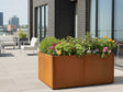 Stor plantekasse i cortenstål fra CUBY fylt med blomster på terrasse
