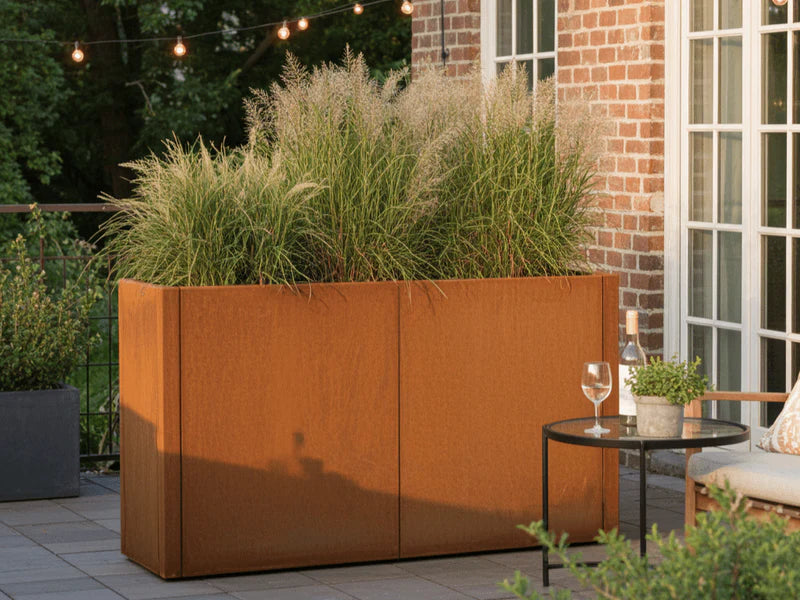 CUBY plantekasse i cortenstål med prydgress på terrasse ved murhus