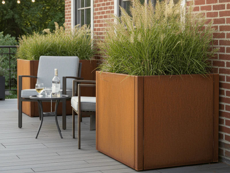 CUBY plantekasse i cortenstål med prydgress på terrasse ved murhus