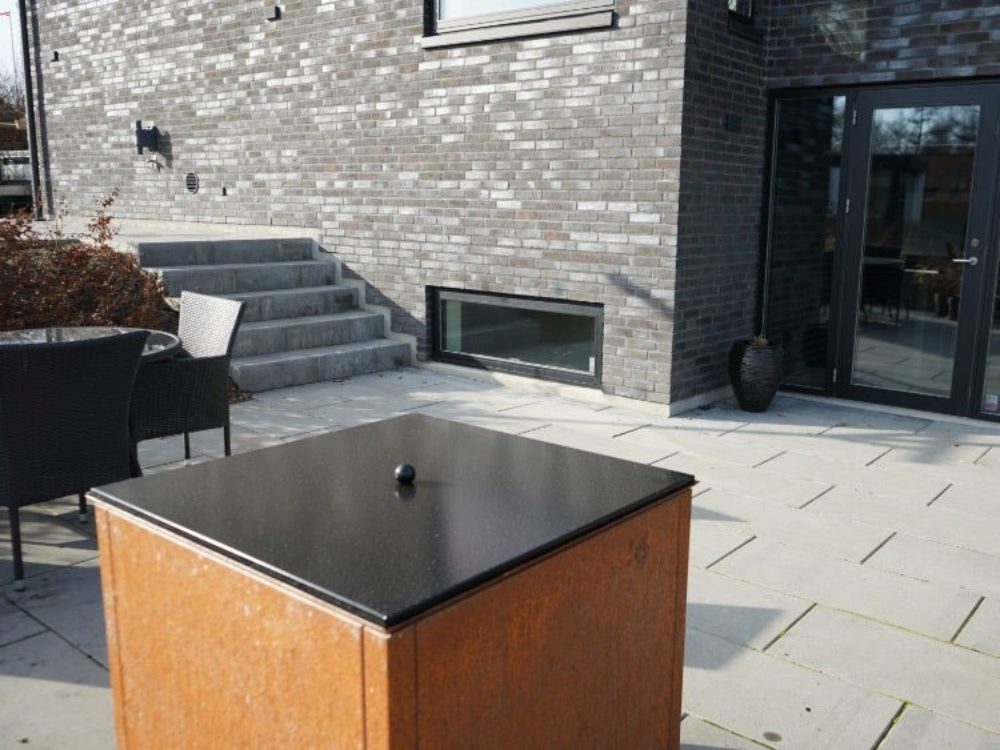 Lokk til bålgrill i svart stål plassert på terrasse