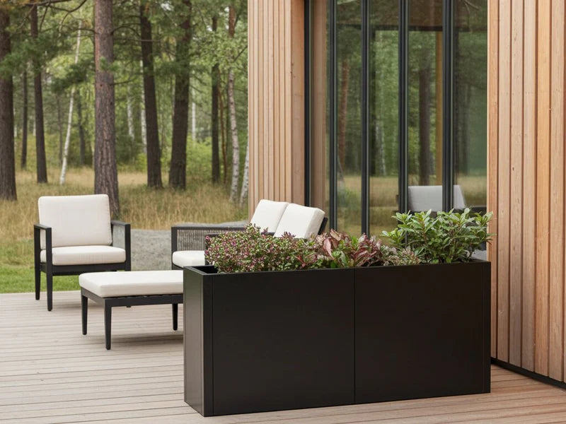 Lang plantekasse i svart stål med stauder ved terrasse