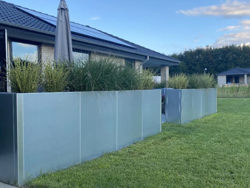 Rekke med plantekasser i galvanisert stål langs plen i moderne hage