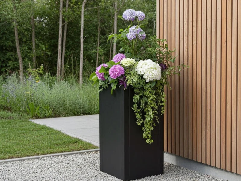 Høy plantekrukke i svart stål med blomstrende planter